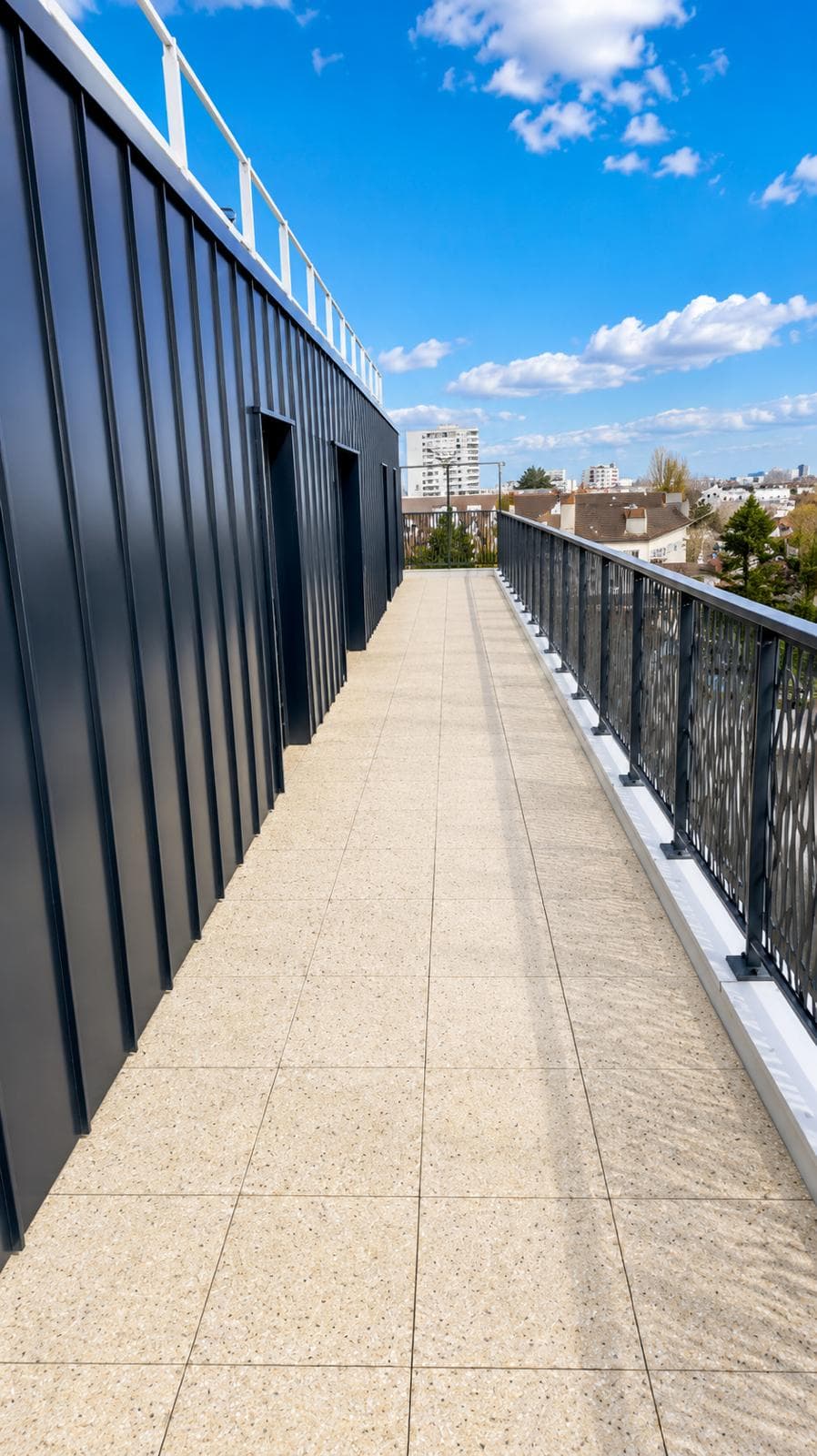 Longue coursive extérieure bordée d'un bardage nervuré anthracite, sur plusieurs dizaines de mètres.