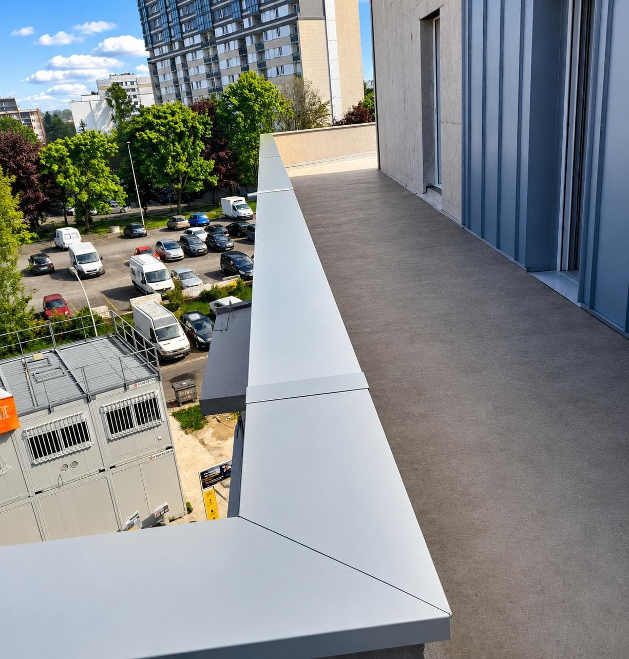 Couvertine en aluminium laqué gris clair posée en tête d'acrotère, avec joints alignés, sur une terrasse d'immeuble.