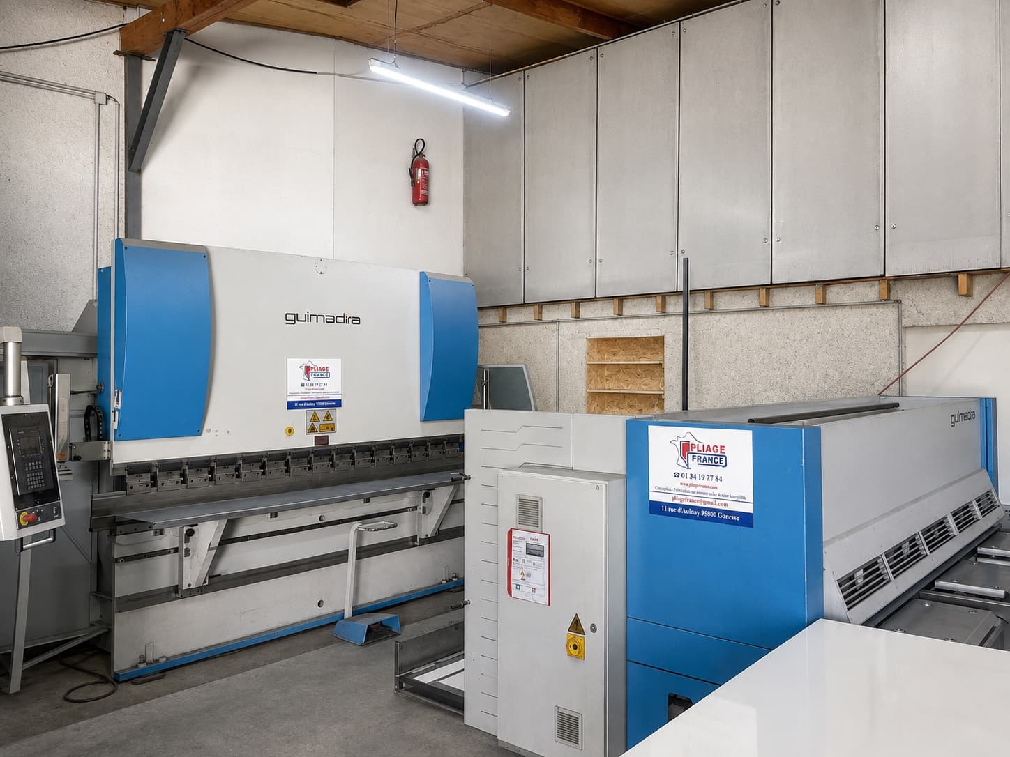Cisaille guillotine bleue portant l'enseigne Pliage France, à côté de la presse plieuse, dans l'atelier.